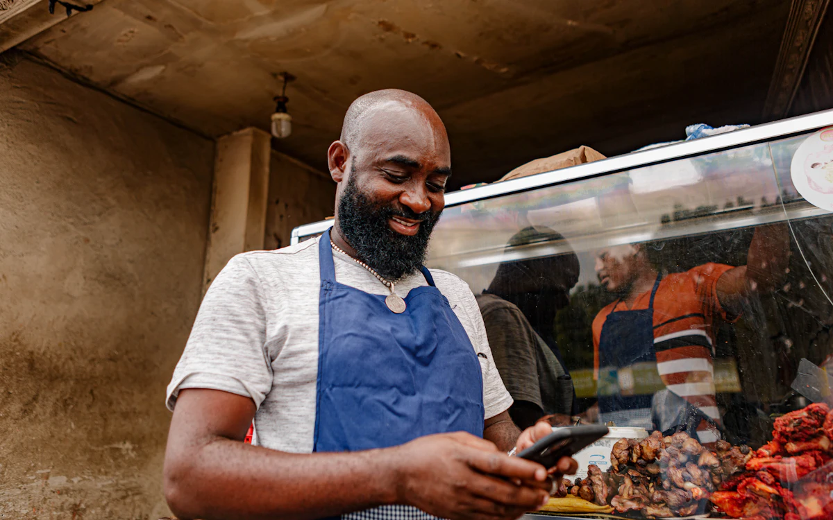 A shop owner in an apron checking messages on his phone